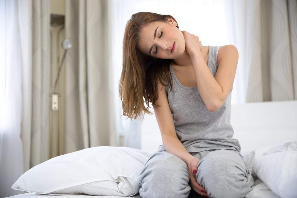 Young woman sitting on the bed with pain in neck